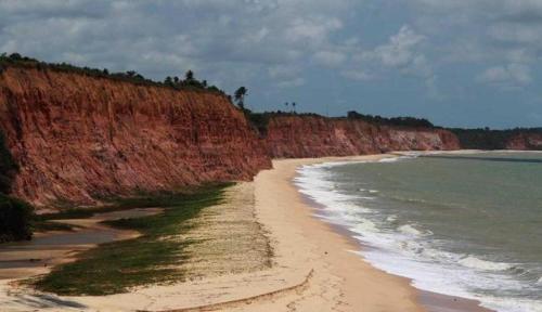 a sandy beach next to the ocean next to a cliff at Quiriri Park Hotel in Prado