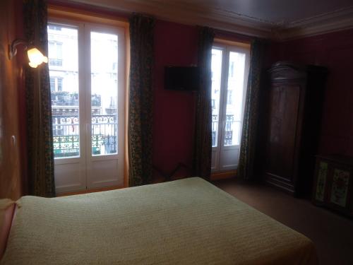 a bedroom with a bed and two windows with a balcony at Hotel des Belges in Paris