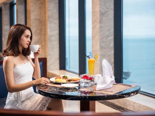 een vrouw aan een tafel met een kopje koffie bij Altara Suites Da Nang by AHG in Da Nang