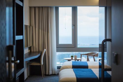 a hotel room with a bed and a desk and a window at Gloucester Hotel Jeju in Jeju