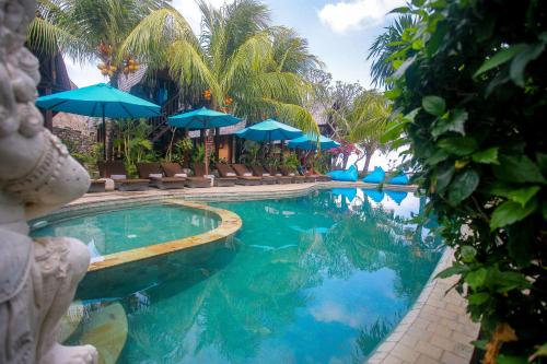 a swimming pool with blue umbrellas and palm trees at Balangan Sea View Bungalow in Jimbaran