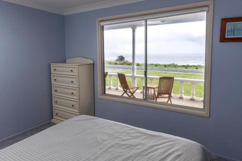 a bedroom with a bed and a window with a table and chairs at Seascape Beach House in Minnie Water
