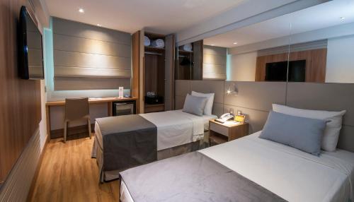 a hotel room with two beds and a desk at Hotel Atlântico Travel Copacabana in Rio de Janeiro