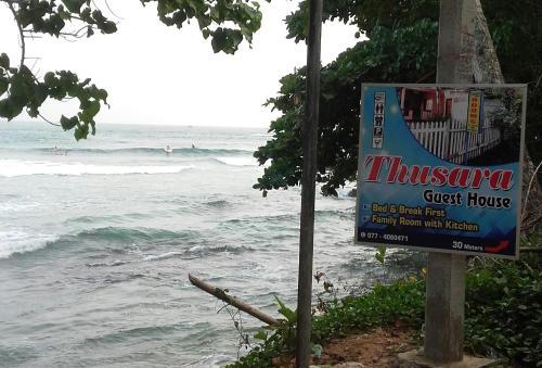 a sign on a pole next to the ocean at Thusara Guesthouse in Mirissa