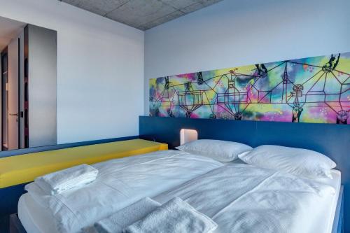 a bedroom with a bed with a painting on the wall at MEININGER Hotel Berlin East Side Gallery in Berlin