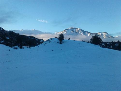 a snow covered hill with trees and a snow covered mountain at Turismo Rural Los Alpes in Futaleufú