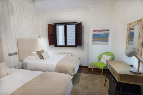 a bedroom with two beds and a desk and a green chair at Cuatro Caminos Rooms in Torrelavega