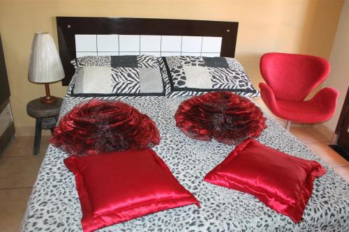 a bed with two red pillows and a red chair at Pousada da Lenna in Rio das Ostras