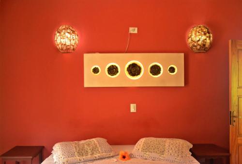 a bedroom with a red wall with a bed and two lights at Pousada Casa de Pedra in Boicucanga
