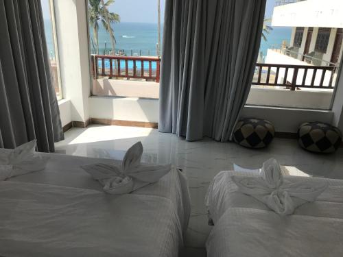 two beds in a room with a view of the ocean at New Ocean Hill Hotel in Hikkaduwa
