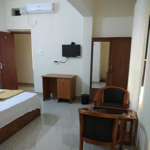 a bedroom with a bed and a chair and a tv at Manjira Lodge in Guruvāyūr