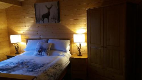 a bedroom with a bed with two lamps and a deer picture on the wall at Lochinvar - Highland Log Cabin with Private Hot Tub in Airdrie