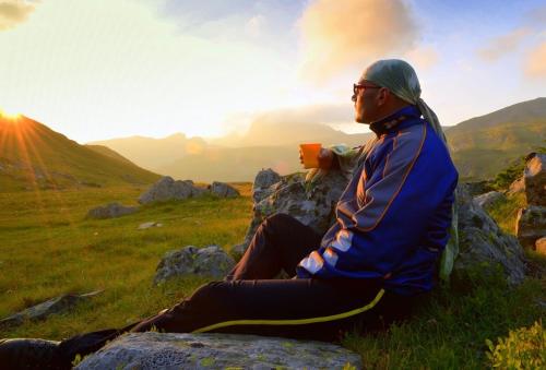 a man sitting on a hill taking a picture of the sunset at Къща за гости "Стария Сом" in Vardim