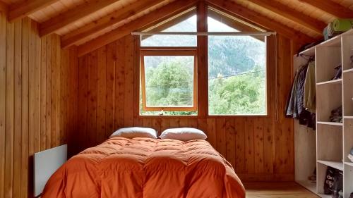 Cama naranja en habitación con ventana en Cabaña Rufus en Lago Puelo
