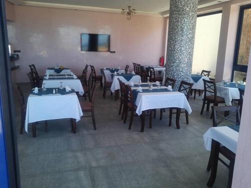 a dining room with white tables and chairs and a tv at Le temps perdu in Oualidia