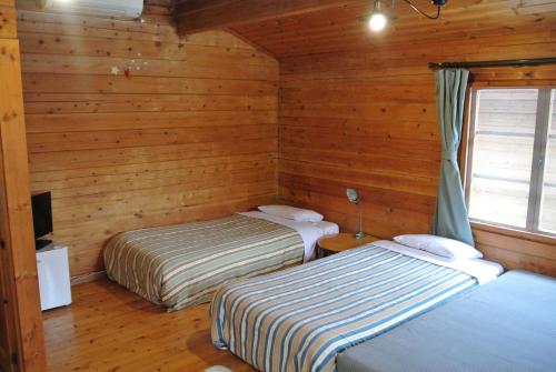 two beds in a room with wooden walls at Polan no Fue in Minamioguni