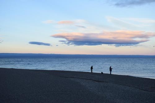 two people and a dog standing on the beach at Hotel Mora in Los Antiguos
