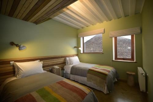 a bedroom with two beds and two windows at Hotel Vendaval in Puerto Natales