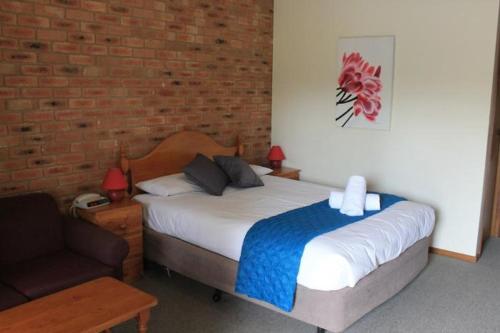 um quarto com uma cama, uma cadeira e uma parede de tijolos em Aristocrat Waurnvale em Geelong