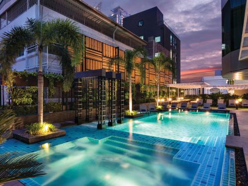 a swimming pool with palm trees in front of a building at Solitaire Bangkok Sukhumvit 11 in Bangkok