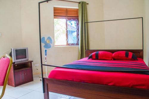 Schlafzimmer mit einem roten Bett und einem TV in der Unterkunft Wal Ville Suites in Gulu