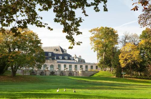 a large house on a green lawn with people walking in front at Auberge du Jeu de Paume in Chantilly