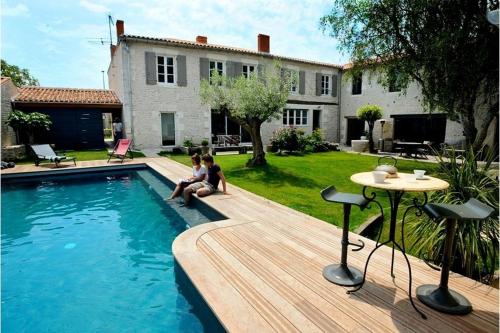 two people sitting on a deck next to a swimming pool at Un Banc au Soleil in Marsilly