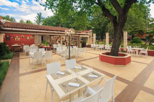 a patio with white tables and chairs and a tree at Istrian Villas Plava Laguna in Umag
