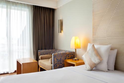 a hotel room with a bed and a chair at Novotel Semarang in Semarang
