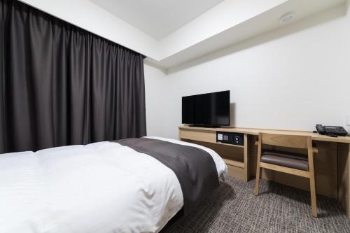 a bedroom with a bed and a desk with a television at Dormy Inn Matsuyama Natural Hot Spring in Matsuyama