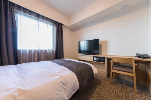 a hotel room with a bed and a desk with a television at Dormy Inn Matsuyama Natural Hot Spring in Matsuyama