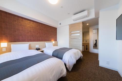 a hotel room with two beds and a flat screen tv at Dormy Inn Matsuyama Natural Hot Spring in Matsuyama