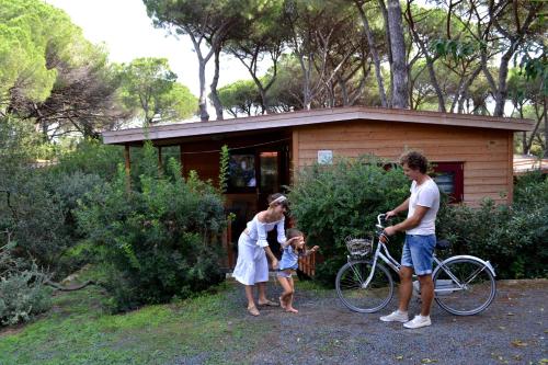 a family standing in front of a house with a bike at Le Esperidi Camping Ecoresort in Marina di Bibbona