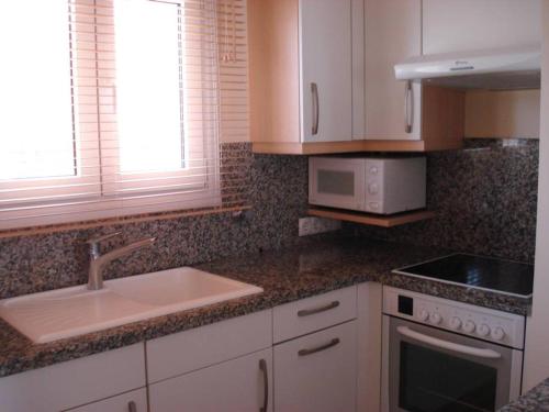 Una cocina con gabinetes blancos, un fregadero y una estufa. en Apartamento entero 3 Habitaciones CLUB SEVILLA III, en Casas Devesa