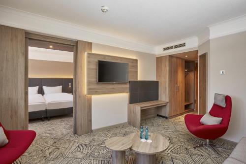a hotel room with a couch and a tv and a bed at H4 Hotel Hannover Messe in Hannover