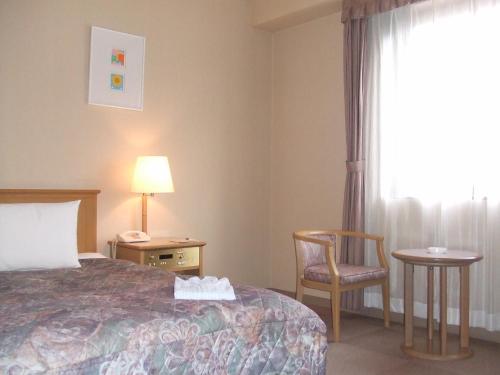 a hotel room with a bed and a chair and a window at Fukuno Town Hotel A・Mieux in Nanto