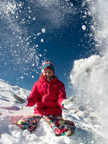 a girl in a red jacket sitting in the snow at Hotel Andreas Hofer in Sankt Leonhard im Pitztal