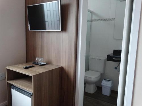 a bathroom with a toilet and a television on the wall at Pousada Natália in Torres