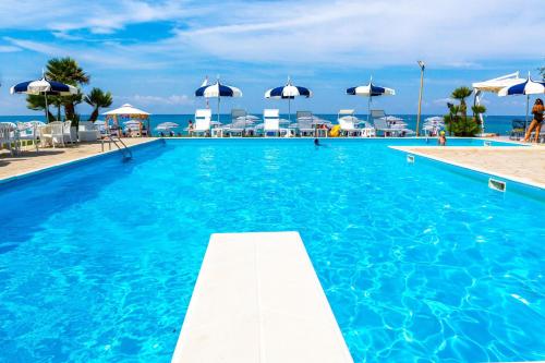 a swimming pool with blue water and chairs and umbrellas at Hotel Poseidon in Diamante