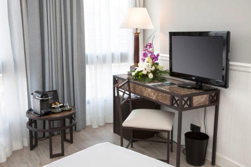 ログローニョにあるHotel Gran Viaのデスク、テレビ、花が備わるホテルルームです。