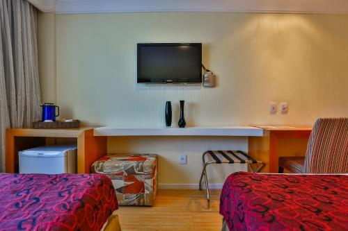 a hotel room with a bed and a tv on the wall at Dubai Macaé by Atlântica in Macaé