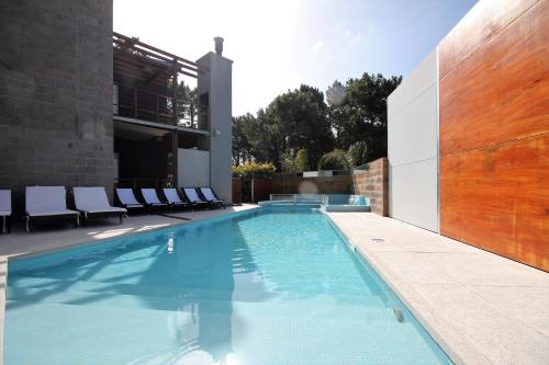 a swimming pool with chairs and a building at La Pedrera in Pinamar
