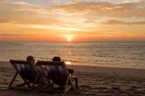 Isara Lanta Beach Resort في كو لانتا: شخصان يجلسون على الكراسي على الشاطئ ويشاهدون غروب الشمس