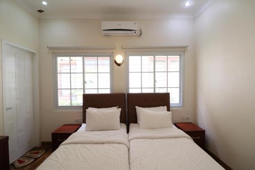 a bedroom with a bed with white sheets and two windows at Diyar Villas Puncak M6/50 in Puncak