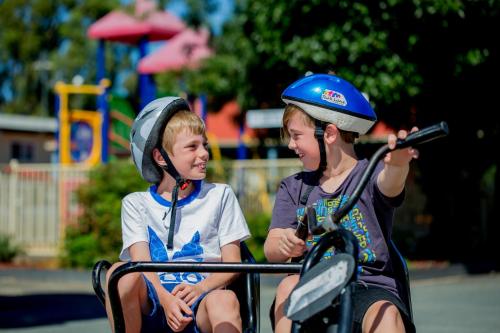 two young boys wearing helmets sitting on a motorcycle at BIG4 Shepparton Park Lane Holiday Park in Shepparton