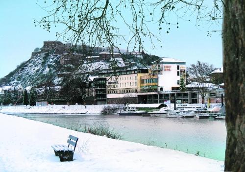 a bench sitting in the snow next to a river at Diehls Hotel in Koblenz
