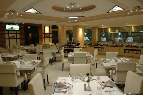 un restaurant avec des tables et des chaises blanches et des personnes dans la cuisine dans l'établissement Sandesh Pride, à Mysore