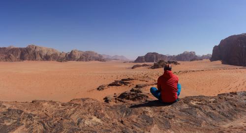 a man sitting on a rock in the desert at Wadi Rum Quiet Village Camp in Wadi Rum