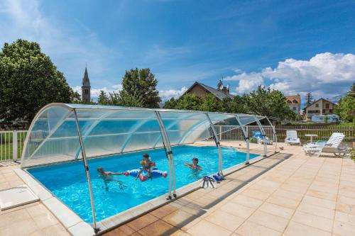 un groupe de personnes se baignant dans une piscine avec une enceinte en verre dans l'établissement Hotel restaurant Le Chamois, à Ancelle