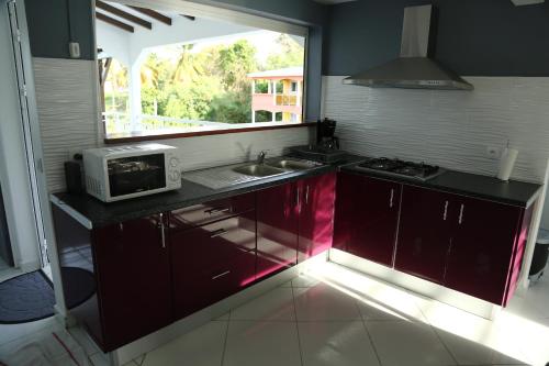 a kitchen with red cabinets and a microwave on a counter at Chez Roberto Bungalow Ayden in Petit-Canal